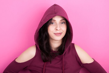 Woman with natural smile wearing a hood on pink background in studio