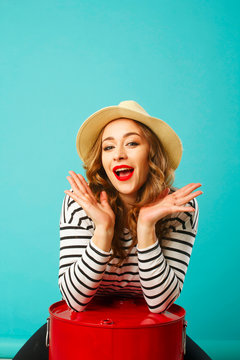 Portrait of young beautiful blond woman in hat with flirting expression on her face over blue background