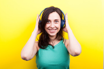 Excited woman listening to music in her blue headphones on yellow background in studio