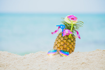Purple orchid flower put on Fresh pineapple juice and sliced pineapple fruit with sunglass on beach and green and blue sea background Summer fruit drink concept.
