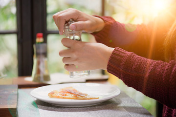 Woman hands using black pepper and salt shaker on the slices of pizza