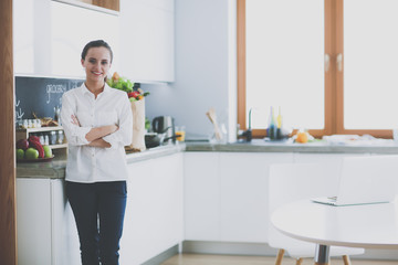 Portrait of young woman standing with arms crossed against kitchen background. Woman in the kitchen.