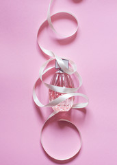 women's perfume in the bottle  intertwined with a gently pink ribbon. delicate pink background