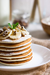 Stack of delicious pancakes with chocolate, honey, nuts and slices of banana and stawderry jam on plate and napkin on wooden background