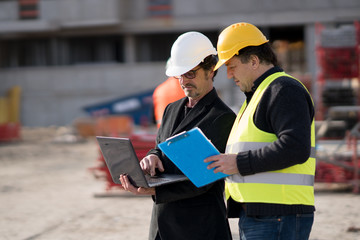 Fototapeta premium Civil engineer giving instructions to a construction worker using a computer laptop. Outdoors