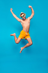 Obraz premium Fullbody, full length portrait of attractive, successful, cheerful, foolish, comic ladies' man in yellow shorts, jumping with open mouth and raised hands, isolated on blue background
