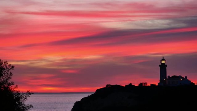 sunset painting the sky in several shades of red with lighthouse silhouette, Carvoeiro, Algarve, Portugal