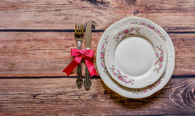 Vintage silverware tied with pink bow and chine on rustic wooden background