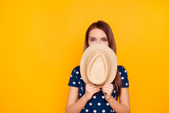 Oops, it is not me. Charming, pretty girl in polka-dot t-shirt close her half face with hat, looking with mad eyes, hiding from someone, watching something, isolated on yellow background