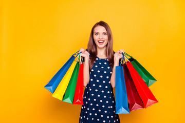 Fototapeta na wymiar Portrait of glad, charming, pretty, crazy girl happy, excited that bought a lot of clothes at low prices, holding packets in two raised hands, isolated on yellow background, unbelievable shopping