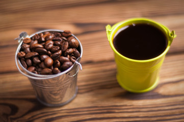 Full green bucket of black coffee near zinked metal bucket with handle full of roasted coffee beans on old worn wooden table