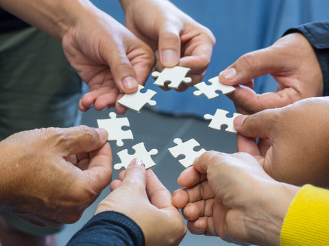 Closeup image of many people hands holding a jigsaw puzzle piece in circle together.