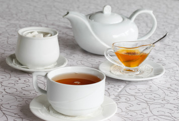 White cup of tea with honey on a white background with teapot. Serving tea. Honey in Saucer.