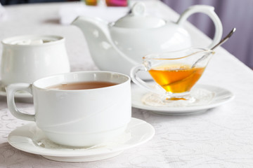 White cup of tea with honey on a white background with teapot. Serving tea. Honey in Saucer.