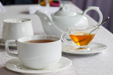 White cup of tea with honey on a white background with teapot. Serving tea. Honey in Saucer.