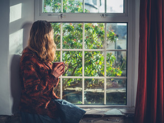 Young woman drinking tea by the window