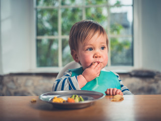 Cute little baby having his dinner at the table - 196162924