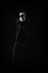 Woman in black leather and sunglasses holding a gun pointed at the camera.