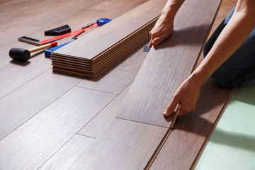 Repairman laying laminate flooring in a home. On the floor lie different carpenter's tools.