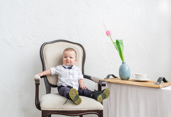  Cute baby boy under 1 year old wearing stylish clothes sitting in vintage chair in home room.