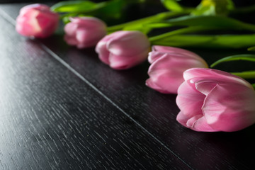 Border from bright pink tulips flowers on black wooden background. Selective focus. Place for text. Flat lay. With an artificial Sun Reflex