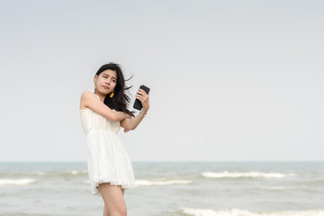 Happy beautiful woman using smartphone for selfie on the beach.