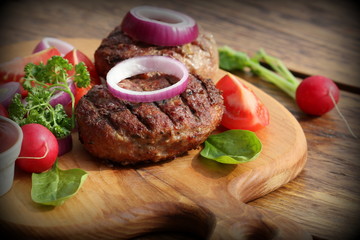 Homemade burger with beef cutlet, vegetables, onion and herbs on wooden cutting board , vintage...