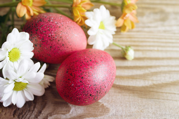 Fototapeta na wymiar Red Easter eggs and flowers of a chrysanthemum on a wooden background, top view, copy space. 