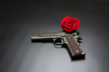 Gun and red rose flower on dark background