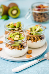 Kiwi granola parfait with nuts and greek yogurt in glass jars. Selective focus, space for text.