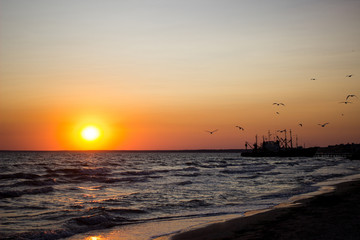 Golden natural sea sunset view of the pier or small bridge on the horizon and orange sky landscape. Sunset or sunrise in nature with the sun in the clouds above the black seascapes.