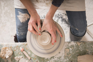 A ceremic artist shaping pottery clay on a pottery wheel in a ceramic workshop.
