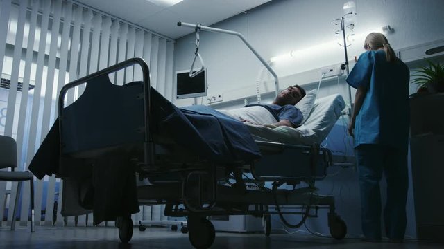 Low Level Shot in the Hospital, Very Sick Man Lying on the Bed, Nurse Checks His Vital Signs and Drop Counter. Shot on RED EPIC-W 8K Helium Cinema Camera.