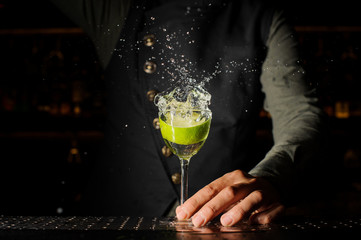 Cocktail glass with splashing alcoholic drink and lime in it