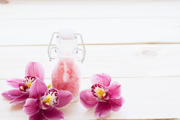Spa and wellness setting with orchid and rose sea salt in a bottle on wooden white background closeup