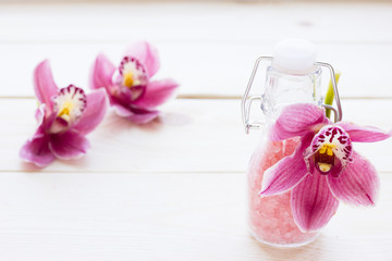 Spa and wellness setting with orchid and rose sea salt in a bottle on wooden white background closeup