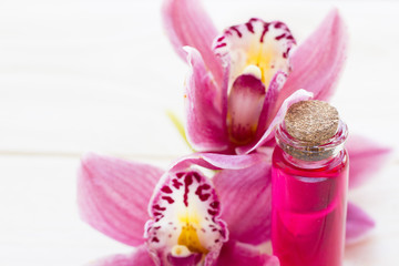 Obraz na płótnie Canvas Spa and wellness setting with orchid and red oil in a bottle on wooden white background closeup