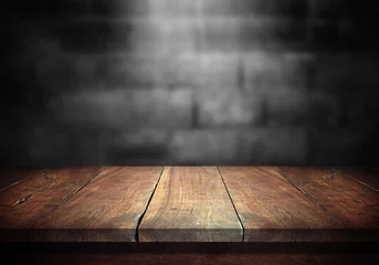 Foto auf Acrylglas Holz Alter Holztisch mit verschwommener Betonblockwand im dunklen Raumhintergrund.