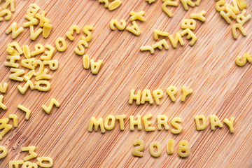 Alphabet pasta forming the text Happy Mothers Day 2018, wood background