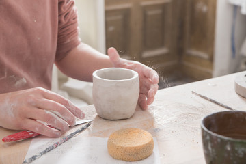 A ceremic artist is putting the finishing touches to a ceramic cup in a pottery workshop.