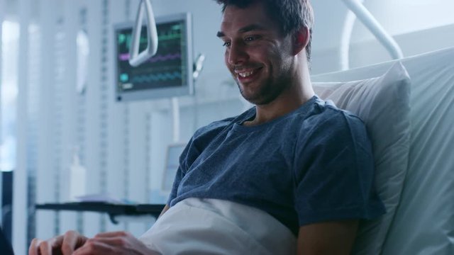 In the Hospital, Sick Male Patient Uses Laptop while Lying on the Bed. Using Technology to Communicate with Loved Ones or do Work. Shot on RED EPIC-W 8K Helium Cinema Camera.