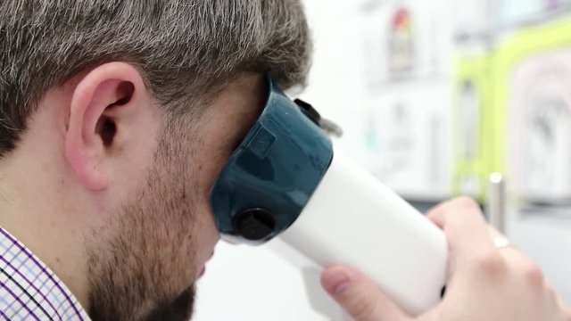 Man looks in apparatus for the treatment of spasm of accommodation, amblyopia and binocular vision disorders. Patient in ophthalmology clinic