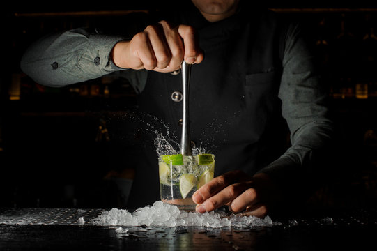 Barman squeezing juice from fresh lime using a citrus press and splashing it out