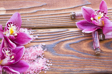 Spa and wellness setting with orchid and rose sea salt and red oil in a bottle on wooden dark background closeup