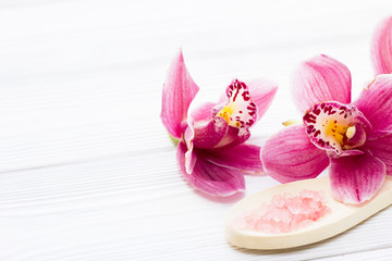 Spa and wellness setting with orchid and rose sea salt on wooden white background closeup