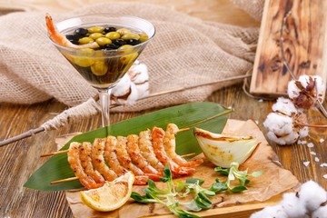 Cold appetizer of shrimps with the original serving of olives in a glass.