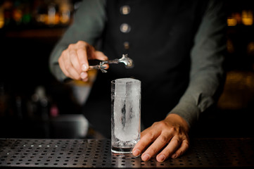 Bartender putting a big rectangular piece of ice into a cocktail glass