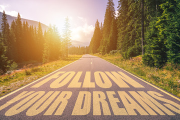 Follow your dreams text written on road in the mountains