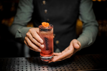 Fototapeta na wymiar Bartender holding a glass with fresh summer light sour cocktail with pink peach liquor decorated with flower