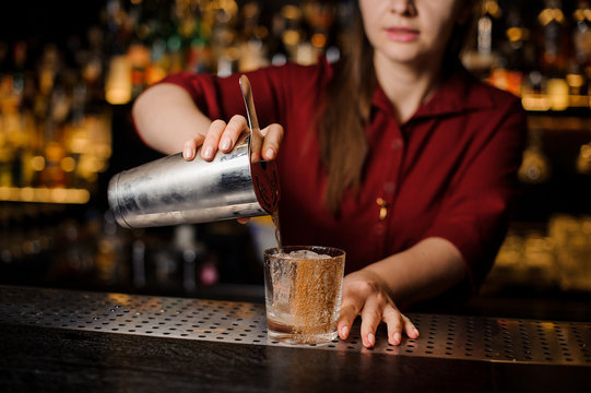 Female bartender pouring a fresh drink from shaker into a glass